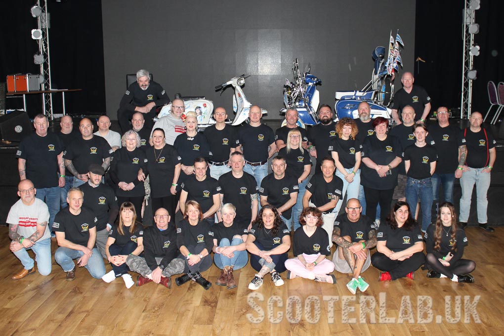 a group photo of The Modrapheniacs Scooter Club taken at the last ever Sandford Scooter Rally in Dorset. pictured with a couple of scooters on the stage.