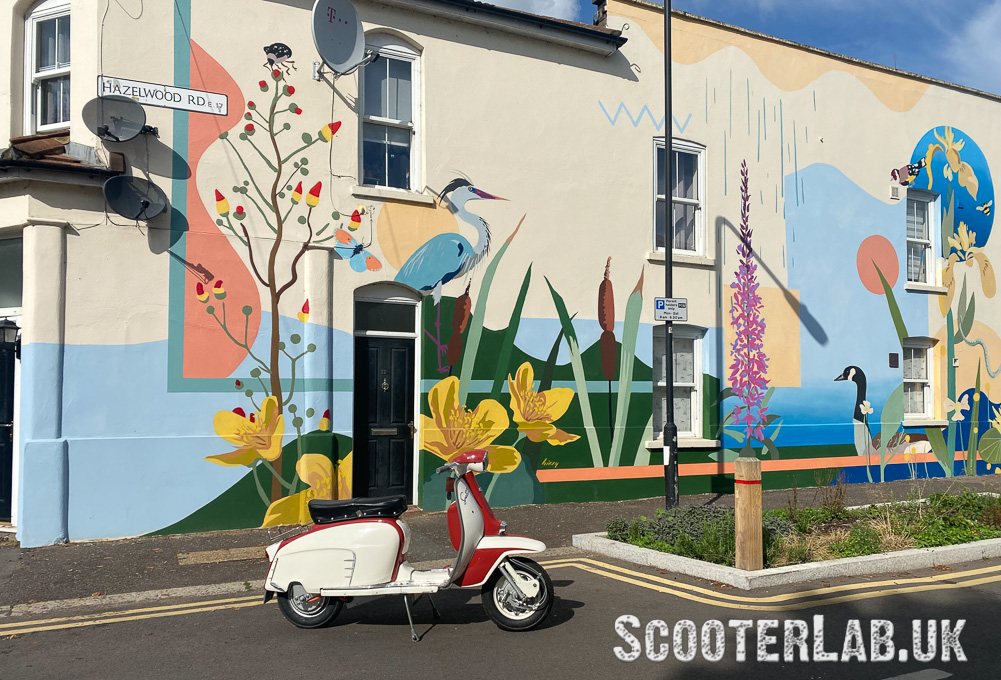 An electric Lambretta parked beside a lovely wall mural in London by the artist,Hizzy